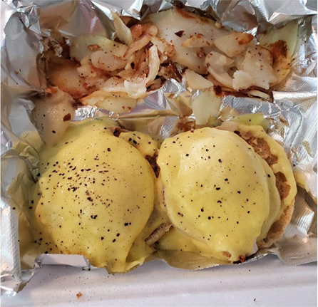 top view close up of eggs benedict and hash browns in take out box